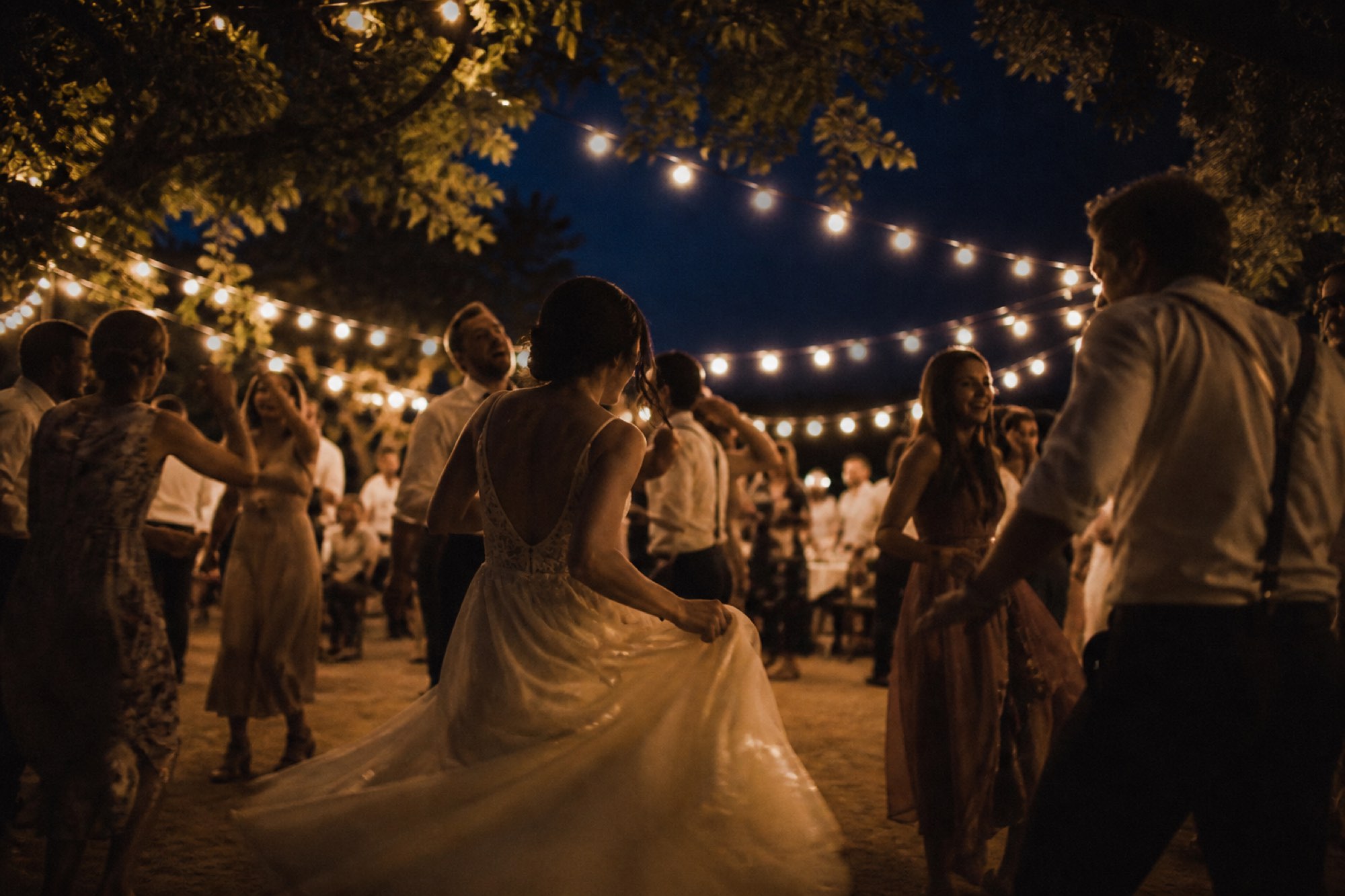 Wedding guests dancing outdoors under warm string lights